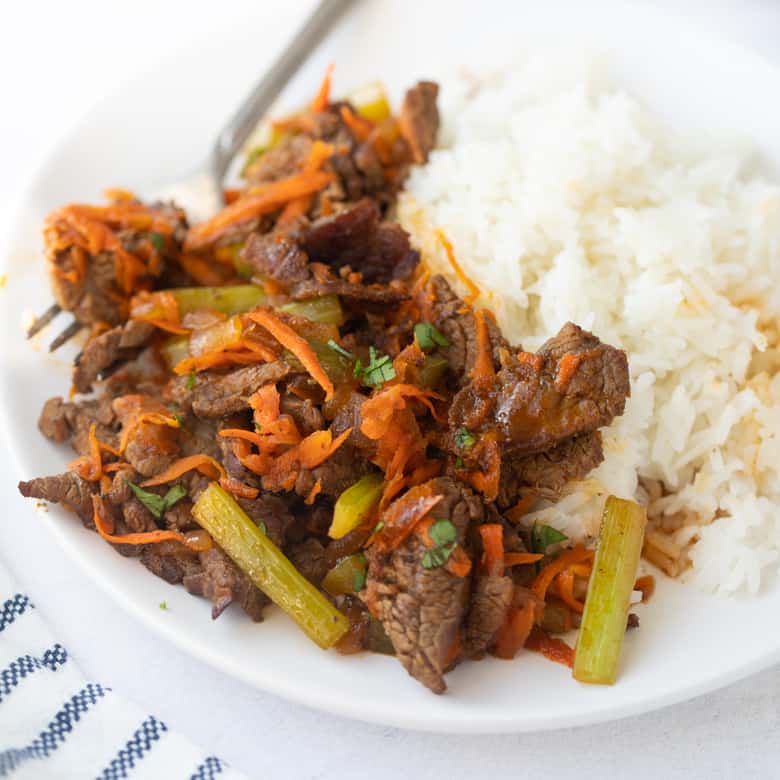 shot of beef stir fry on white plate with rice