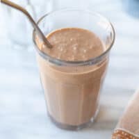 peanut butter banana smoothie in a glass with a metal straw