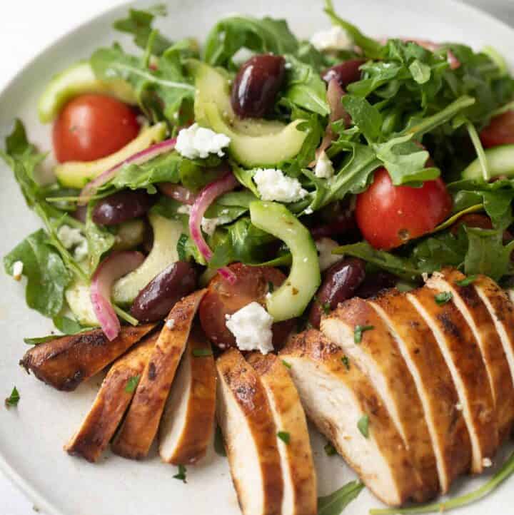 Mediterranean salad on a white plate with slices of grilled chicken breast