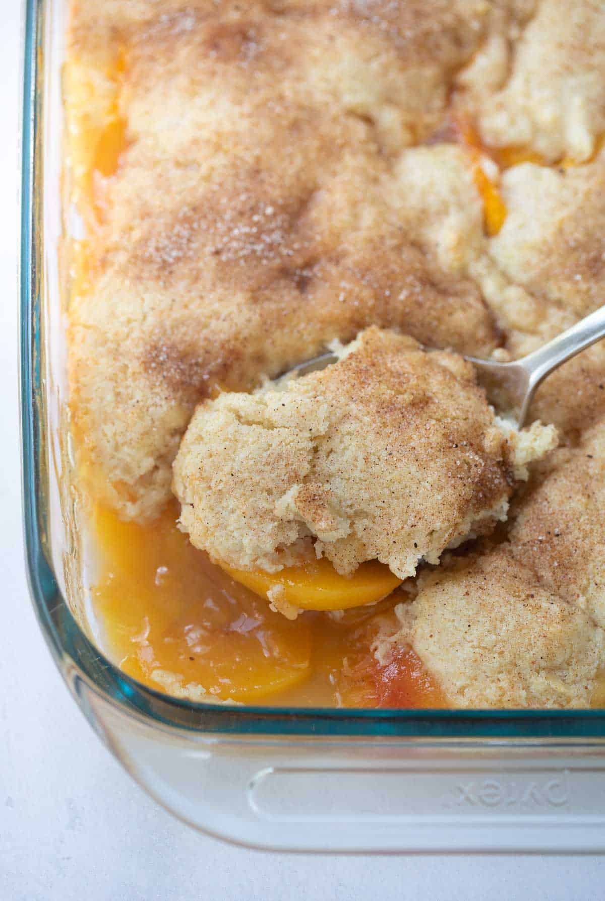 peach cobbler in pan being scooped with a spoon