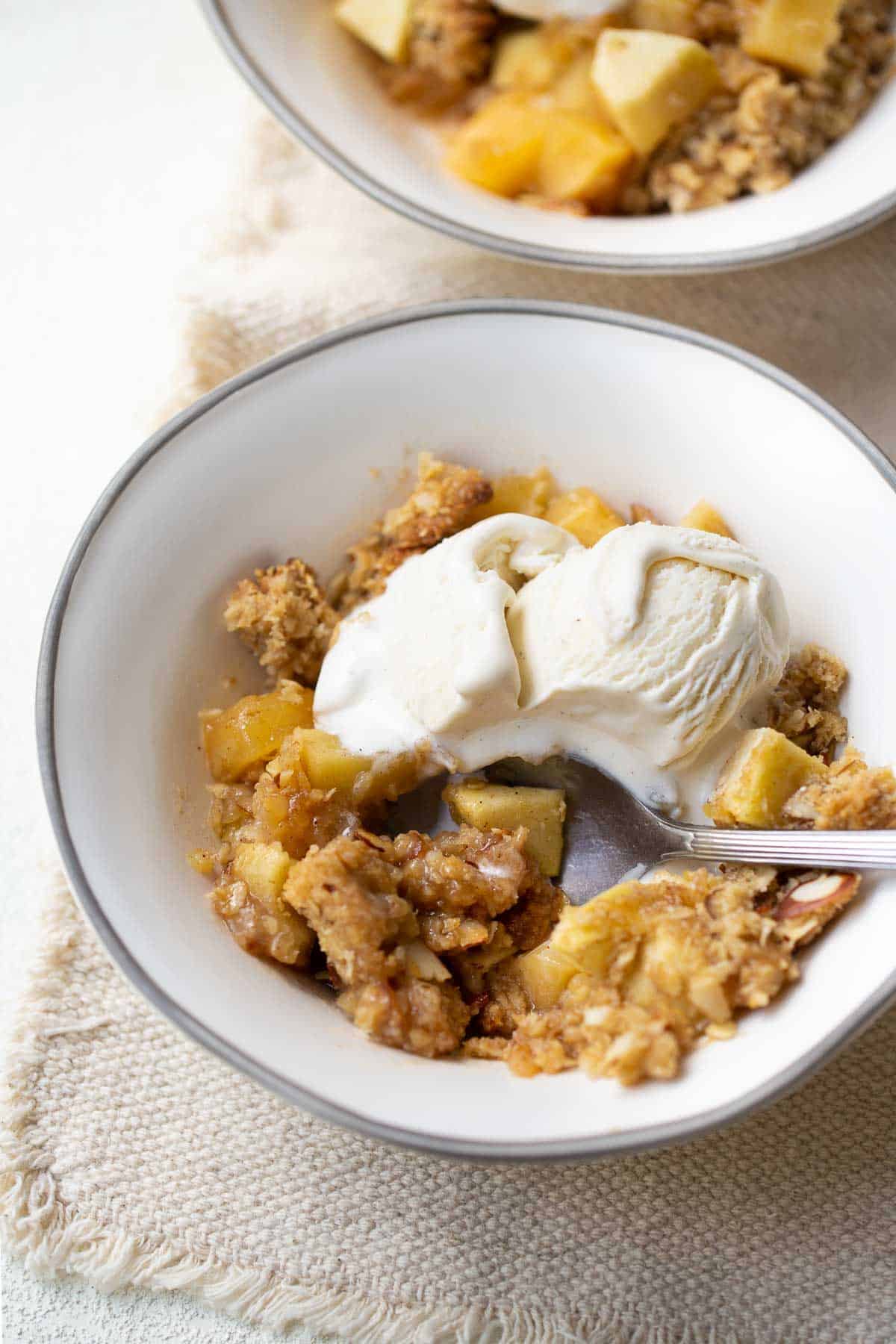 apple crisp in white bowl topped with ice cream and spoon