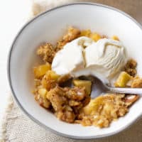 gluten-free apple crisp in white bowl with ice cream and spoon