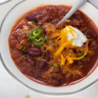 gluten-free chili in white bowl topped with sour cream and cheese