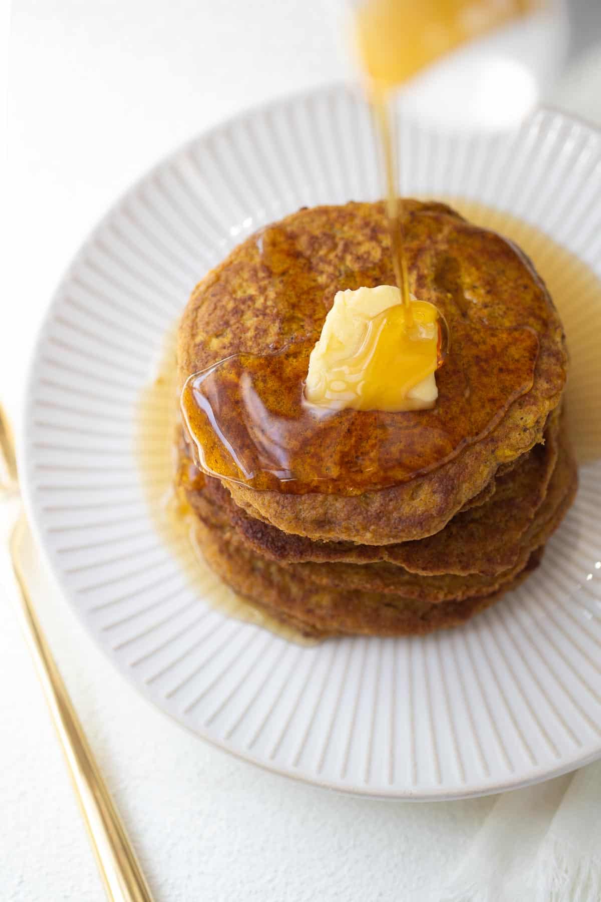 pumpkin oatmeal pancakes on white plate with maple syrup