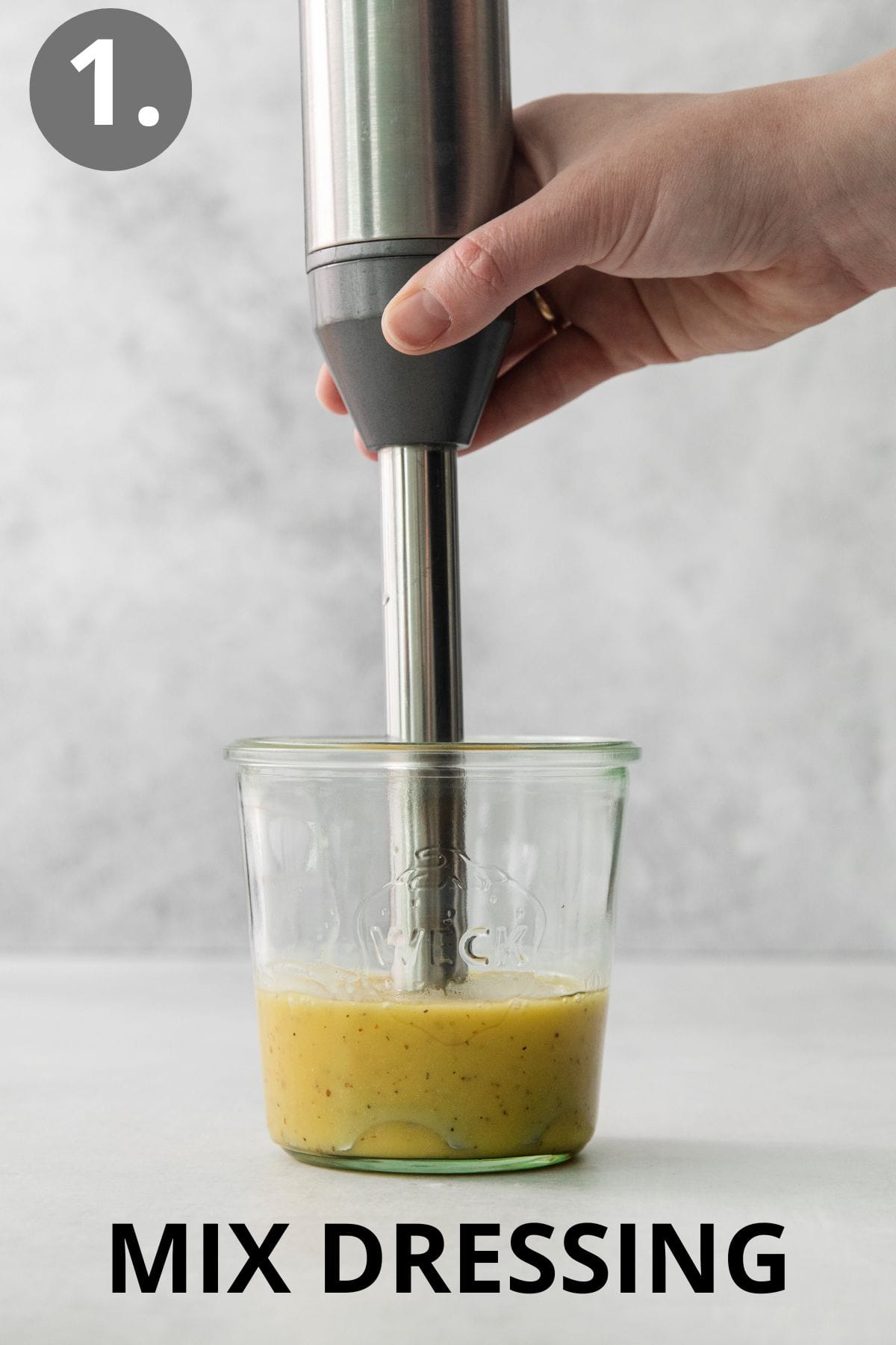 a hand using a hand blender to mix the dressing