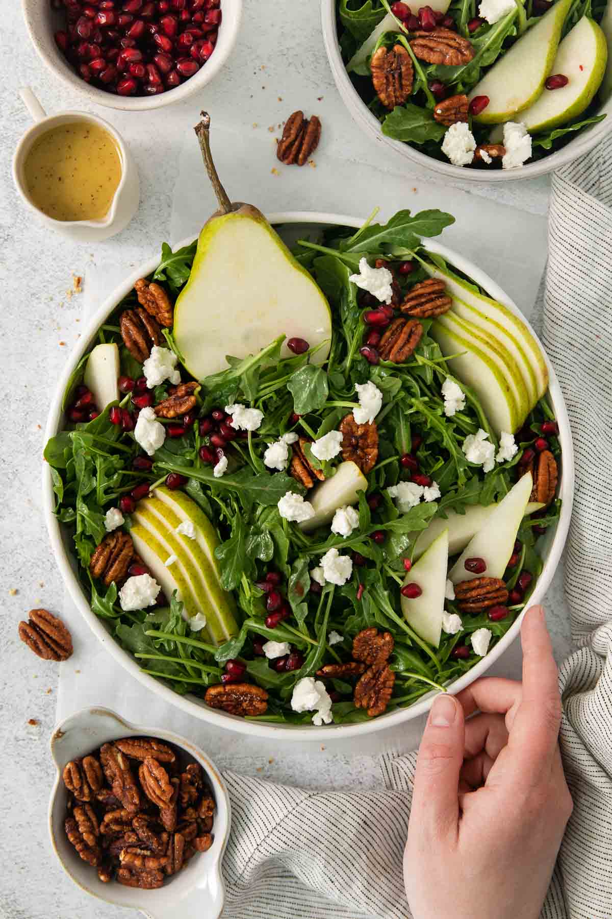 a hand touching the arugula pear salad in a bowl