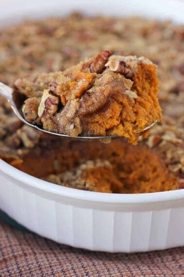 sweet potato casserole being scooped from white casserole dish with red and orange napkin