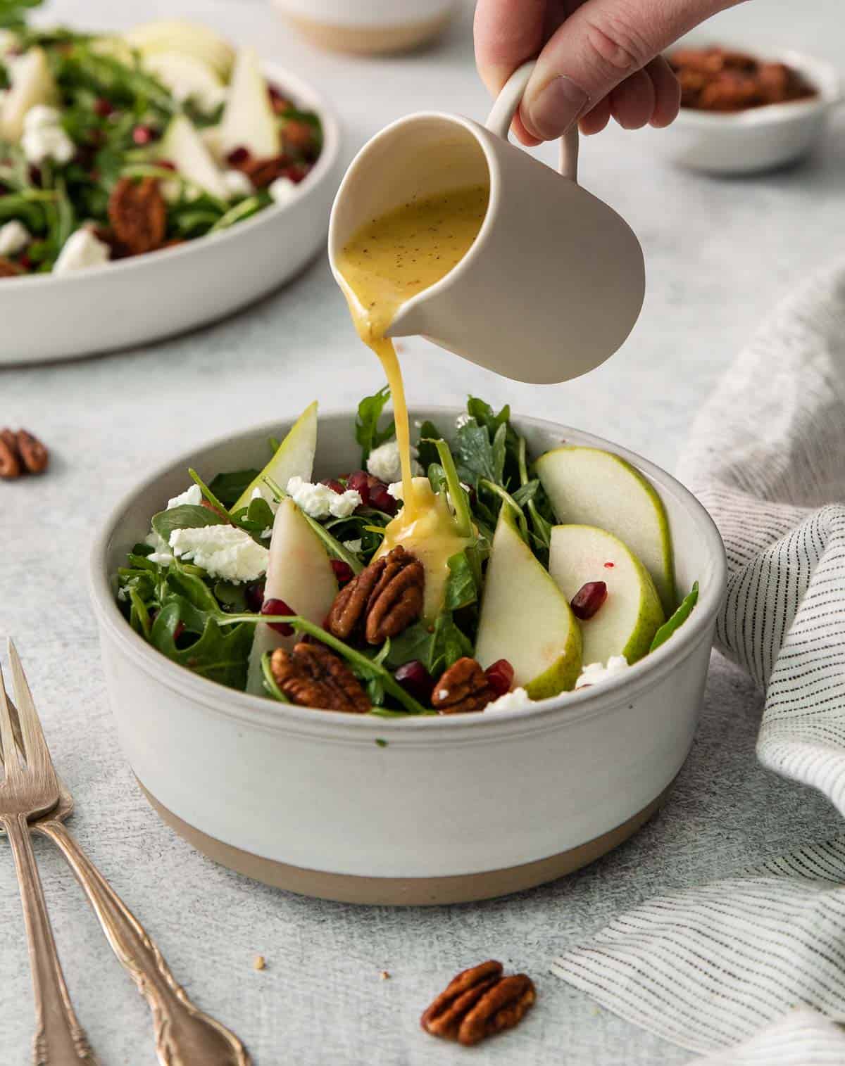 arugula pear salad in a bowl and a hand pouring dressing on top