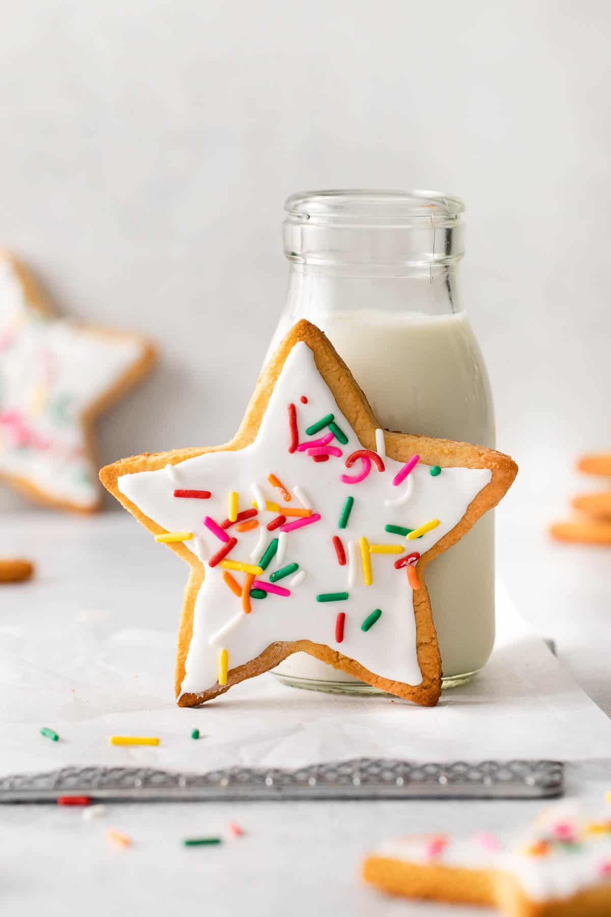 sugar cookie with frosting leaning against jug of milk