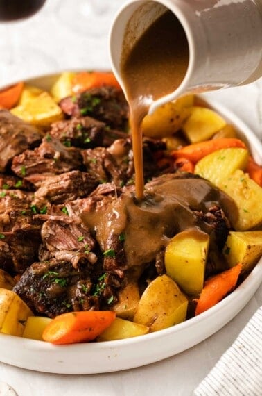 Pot roast on a serving tray with gravy being poured over it