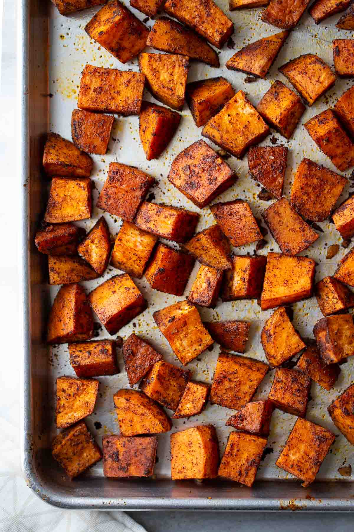 Roasted Sweet Potatoes cubes seasoned with chili powder on pan