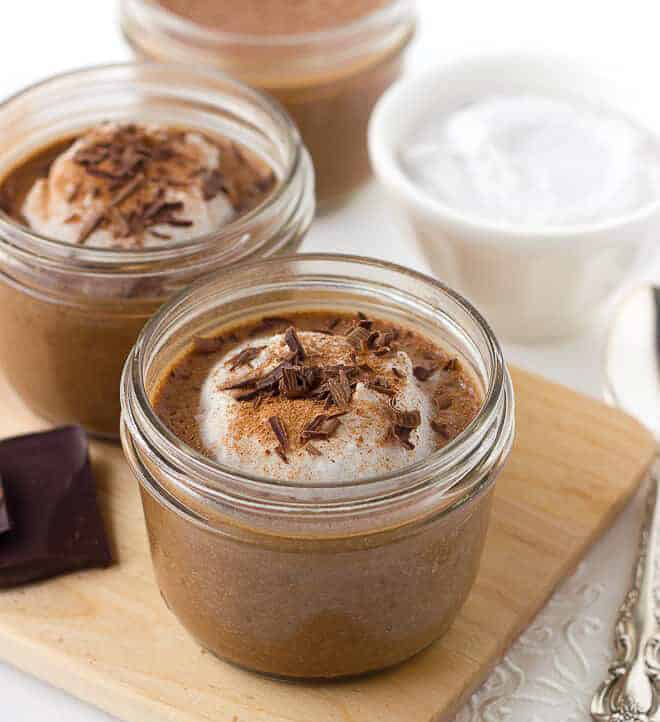 2 servings of chocolate chia pudding garnished with whipped cream and chocolate shavings in 1/2 pint glass jars