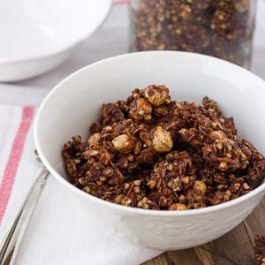 chocolate granola in white bowl with white and red dish towel