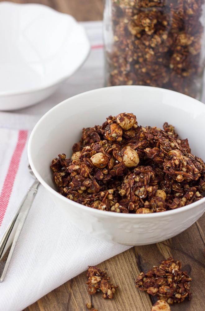chocolate granola in white bowl with white dish towel and spoon