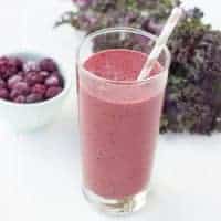 Smoothie in a glass with a straw with a bowl of berries in the background