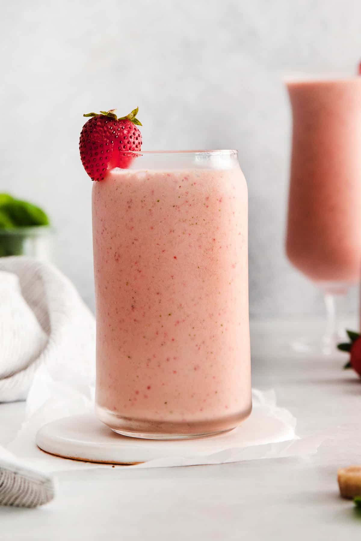 A close up of the strawberry spinach smoothie in a glass with a fresh strawberry on top
