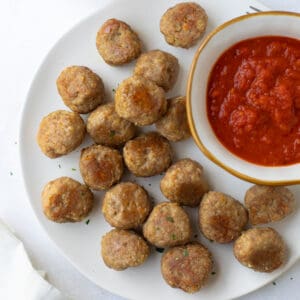 meatballs on white plate with bowl of marinara sauce