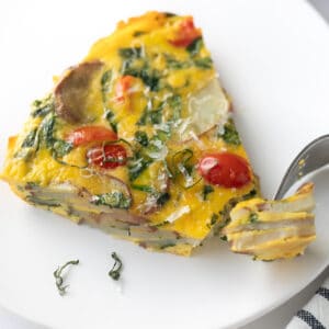frittata on white plate topped with basil and fork