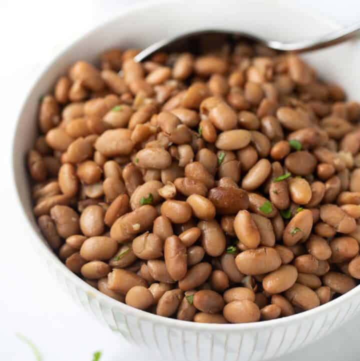 slow-cooker pinto beans in white bowl with serving spoon