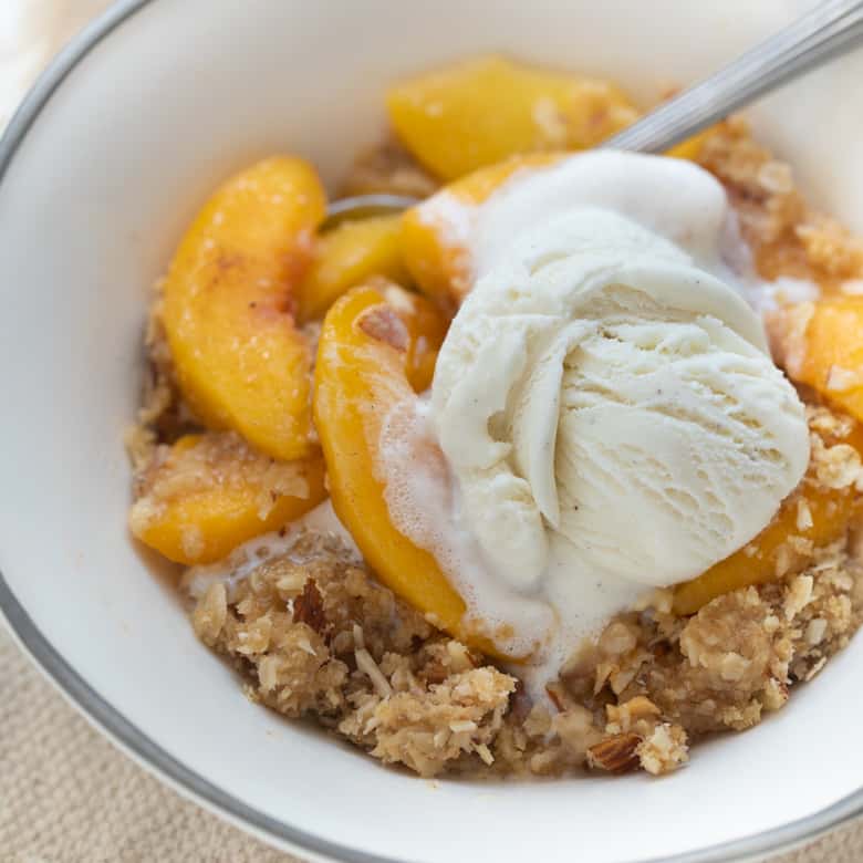 gluten-free peach crisp topped with vanilla ice cream in white bowl