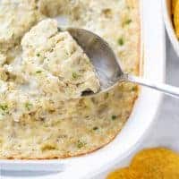 artichoke dip in white baking dish being scooped with spoon