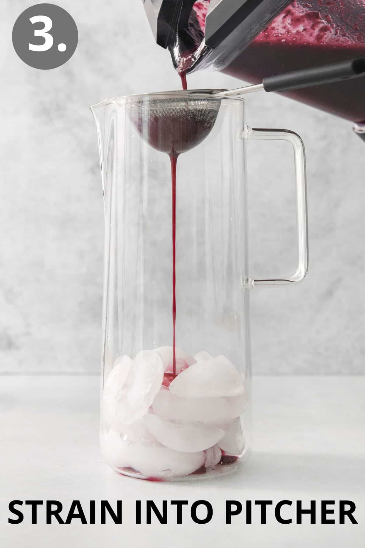 A hand pouring the berry concentrate through a strainer and into a glass pitcher