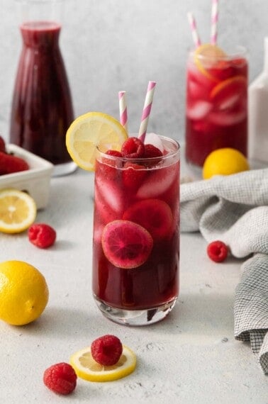 berry lemonade in a glass with two striped straws and a slice of lemon on the side
