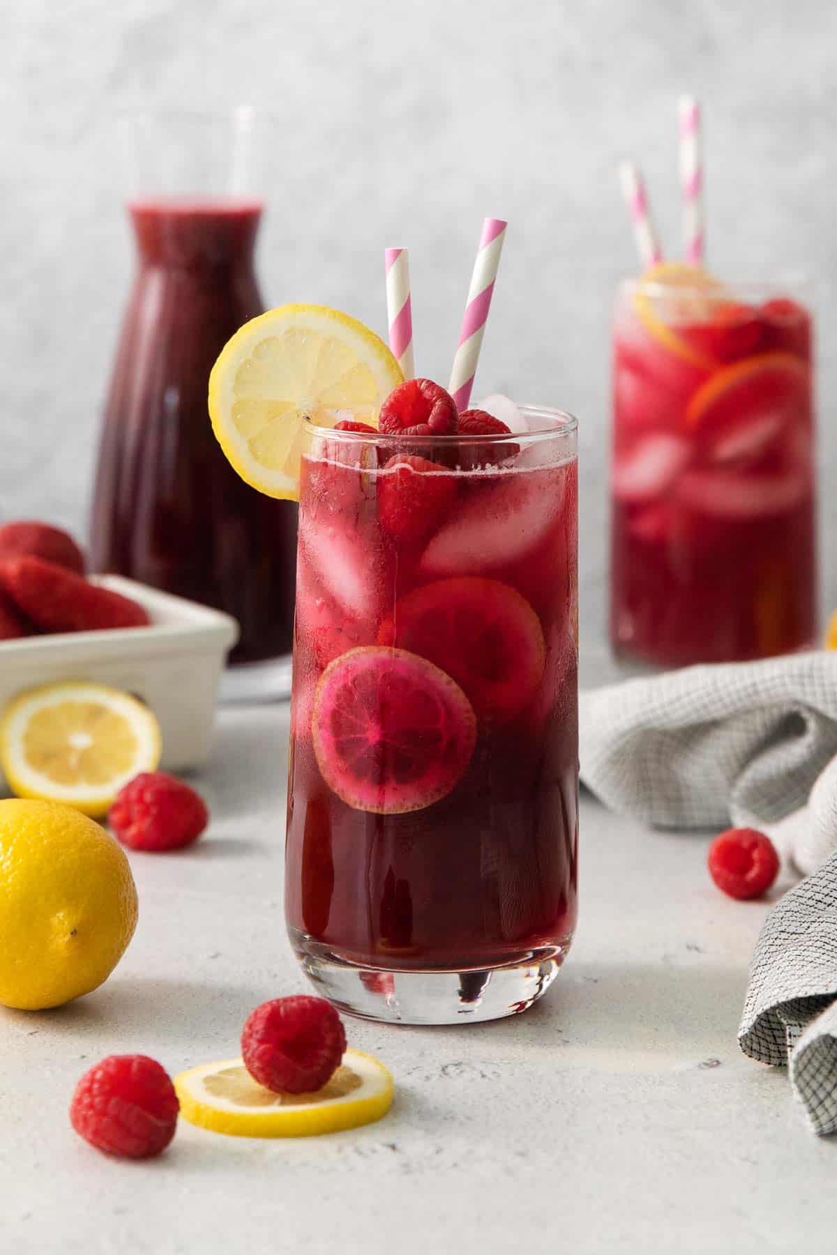 berry lemonade in a glass with two striped straws and a slice of lemon on the side