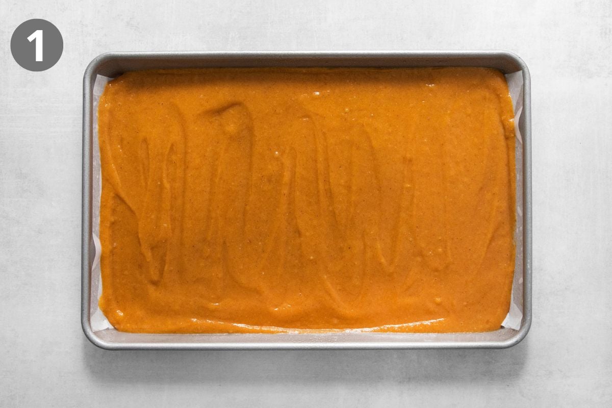 Orange pumpkin cake batter spread evenly into a rectangular parchment-lined baking pan.