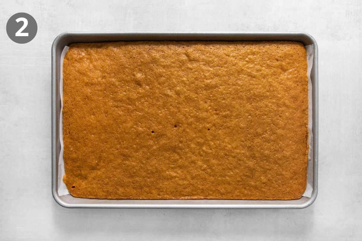 A rectangular baked cake in a parchment-lined metal baking pan.