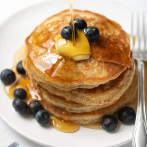 stack of gluten free pancakes with maple syrup and blueberries on white plate