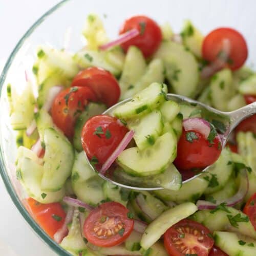 cucumber tomato salad with apple cider vinaigrette on spoon with remaining salad in clear glass bowl