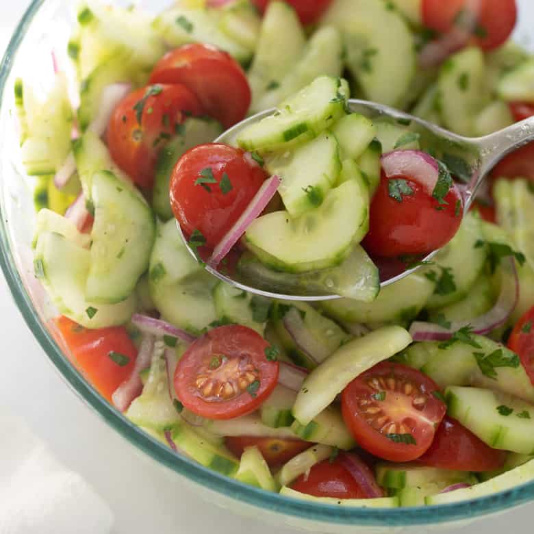 cucumber tomato salad in glass bowl with serving spoon