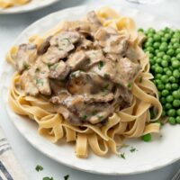 beef stroganoff on white plate topped with parsley and served with peas