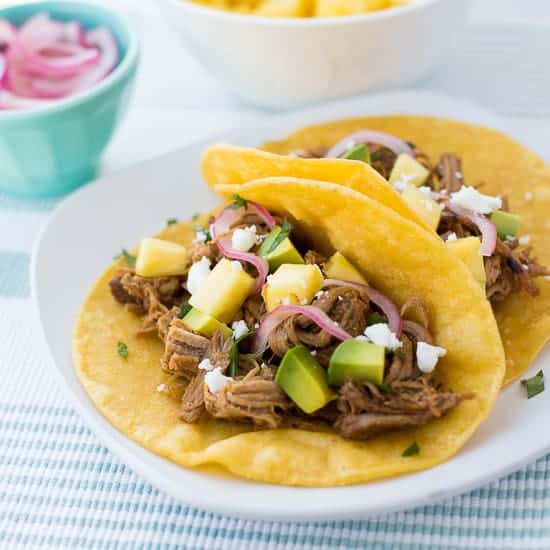 tacos on white plate with blue striped napkin and bowl of pickled onions