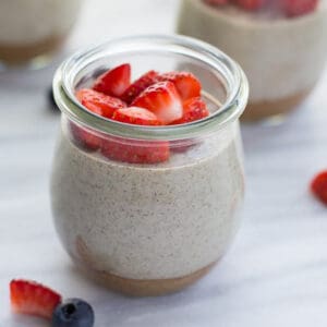 chia pudding in glass jar topped with berries on marble background