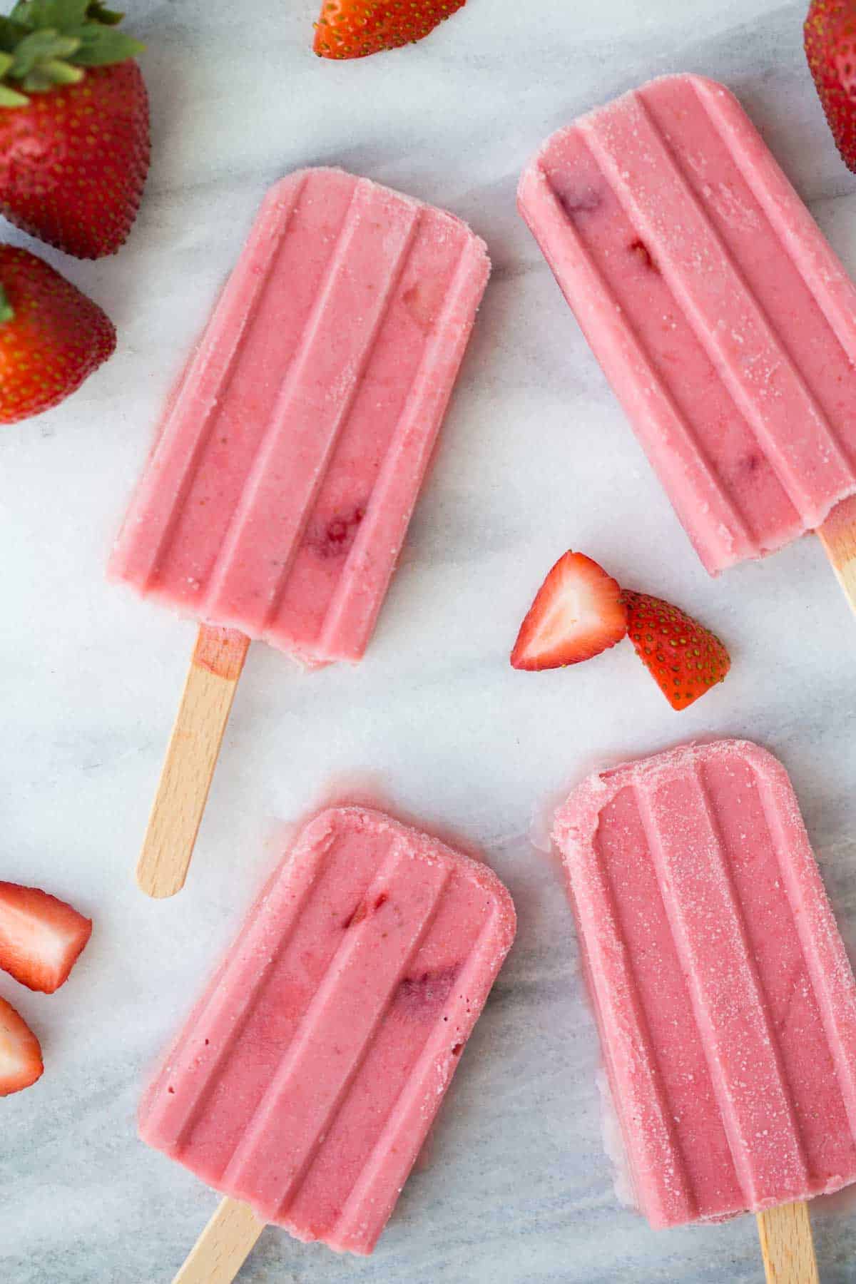 a close up shot of fruit popsicles with strawberries on marble background