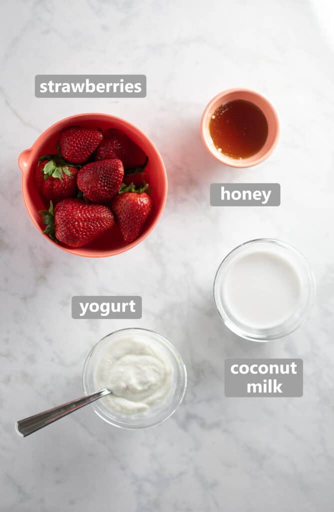 overhead photo: glass bowls with whole strawberries, yogurt, honey, and coconut milk to make a healthy popsicle recipe