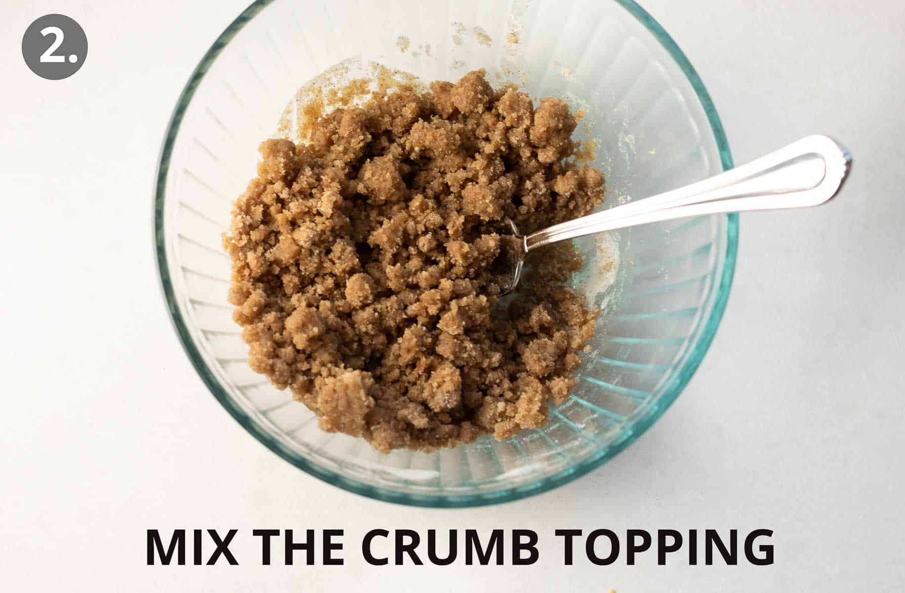 A glass bowl with crumb topping ingredients and a spoon