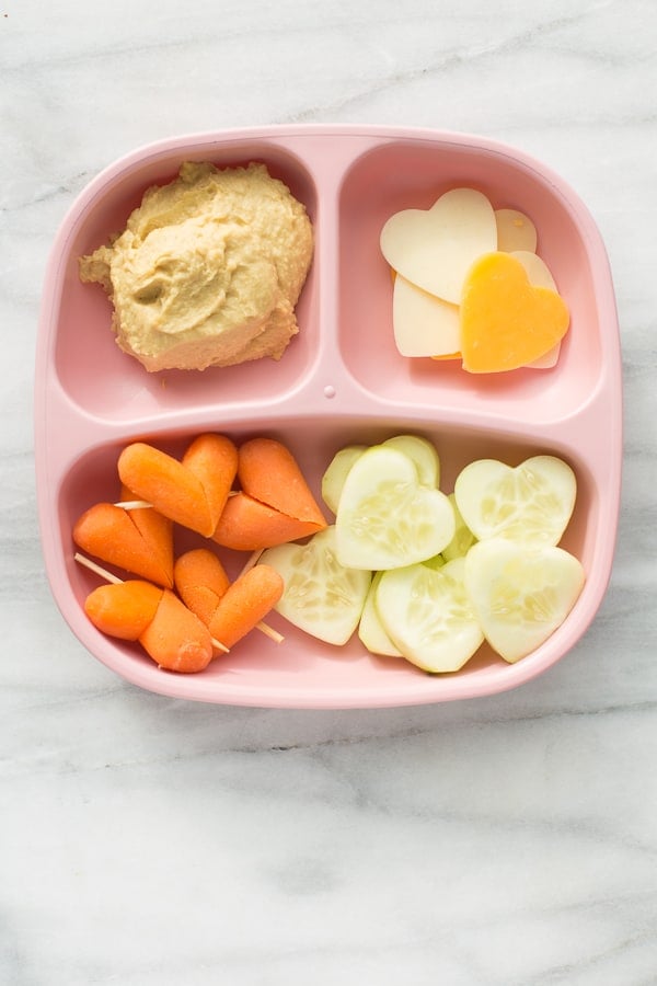 pink plate with heart shaped vegetables and hummus