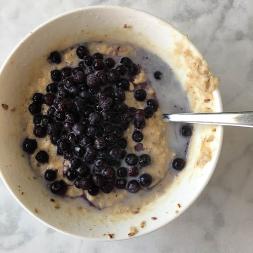 oatmeal in white bowl topped with blueberries and almond milk