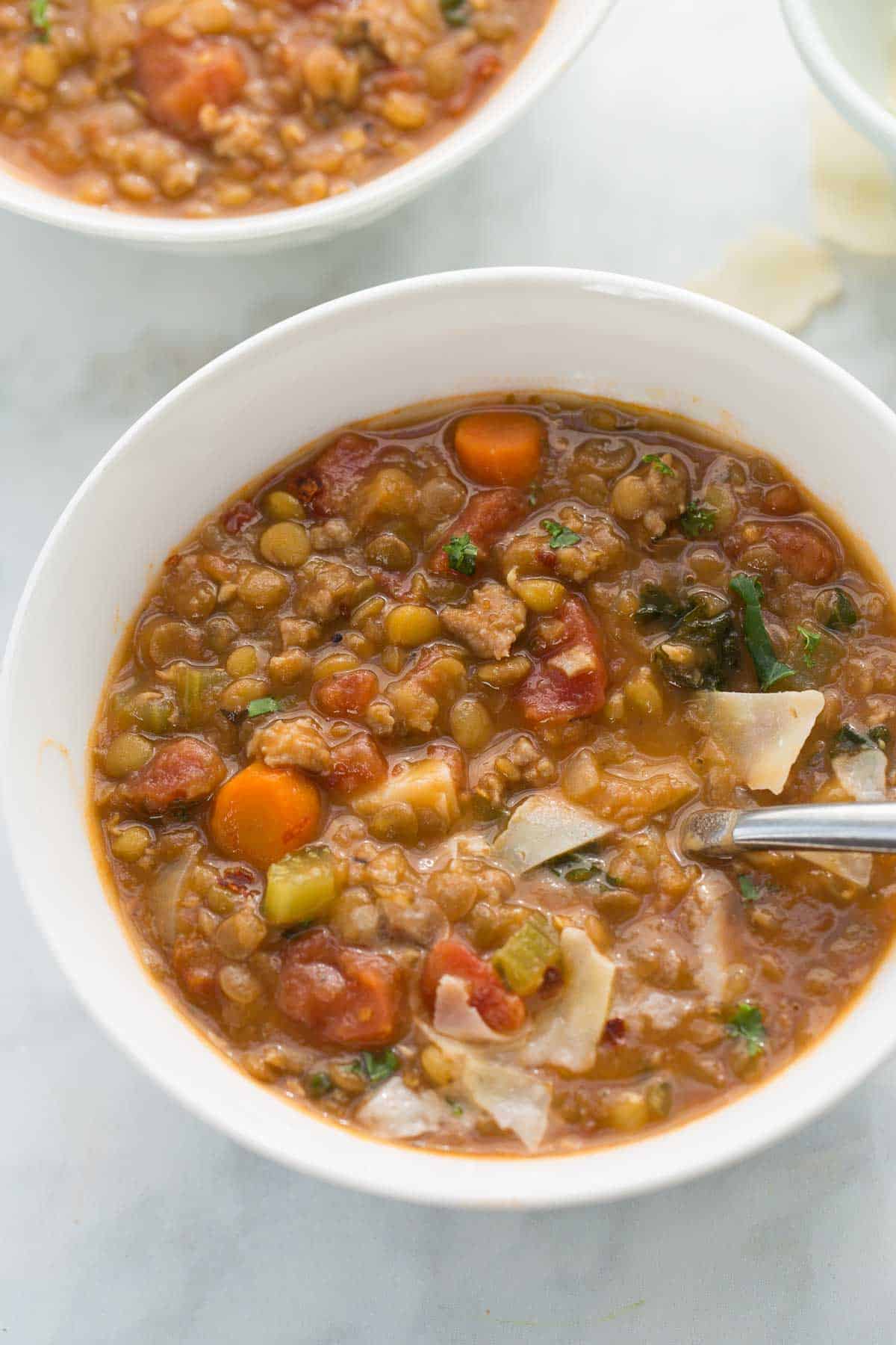 close up of sausage lentil soup in bowl with parmesan