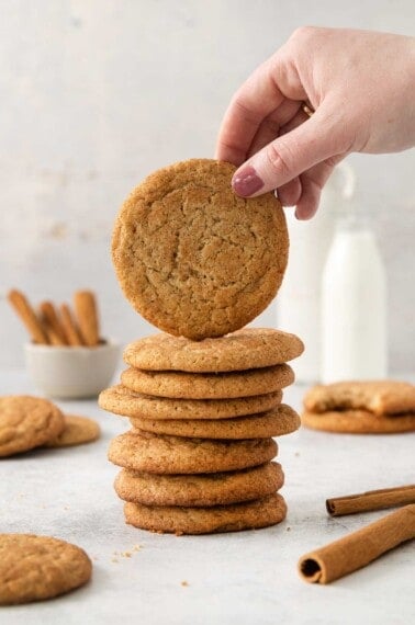 almond flour snickerdoodles stacked on top of each other, and a hand reaching for the top cookie