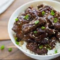 beef teriyaki over rice in white bowl topped with scallions