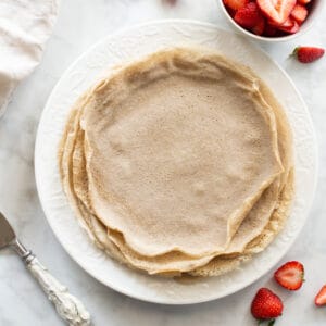 overhead shot of buckwheat crepes on white plate with strawberries