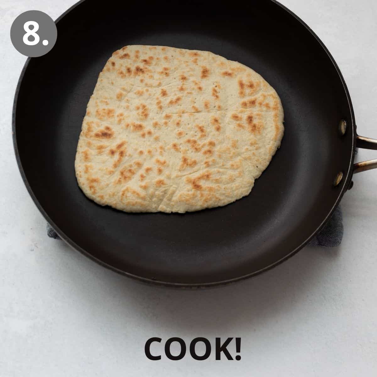 A piece of flatbread down rolled out into a flat circle and cooking in a skillet