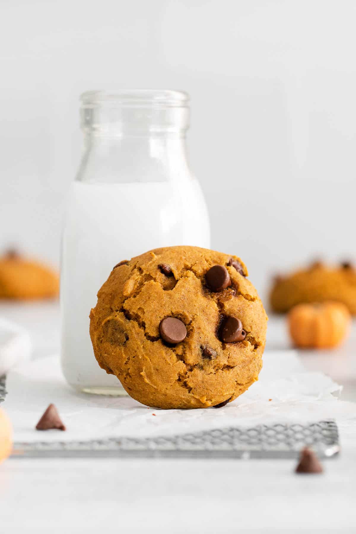 A pumpkin chocolate chip cookie leaning up against a glass jar of milk