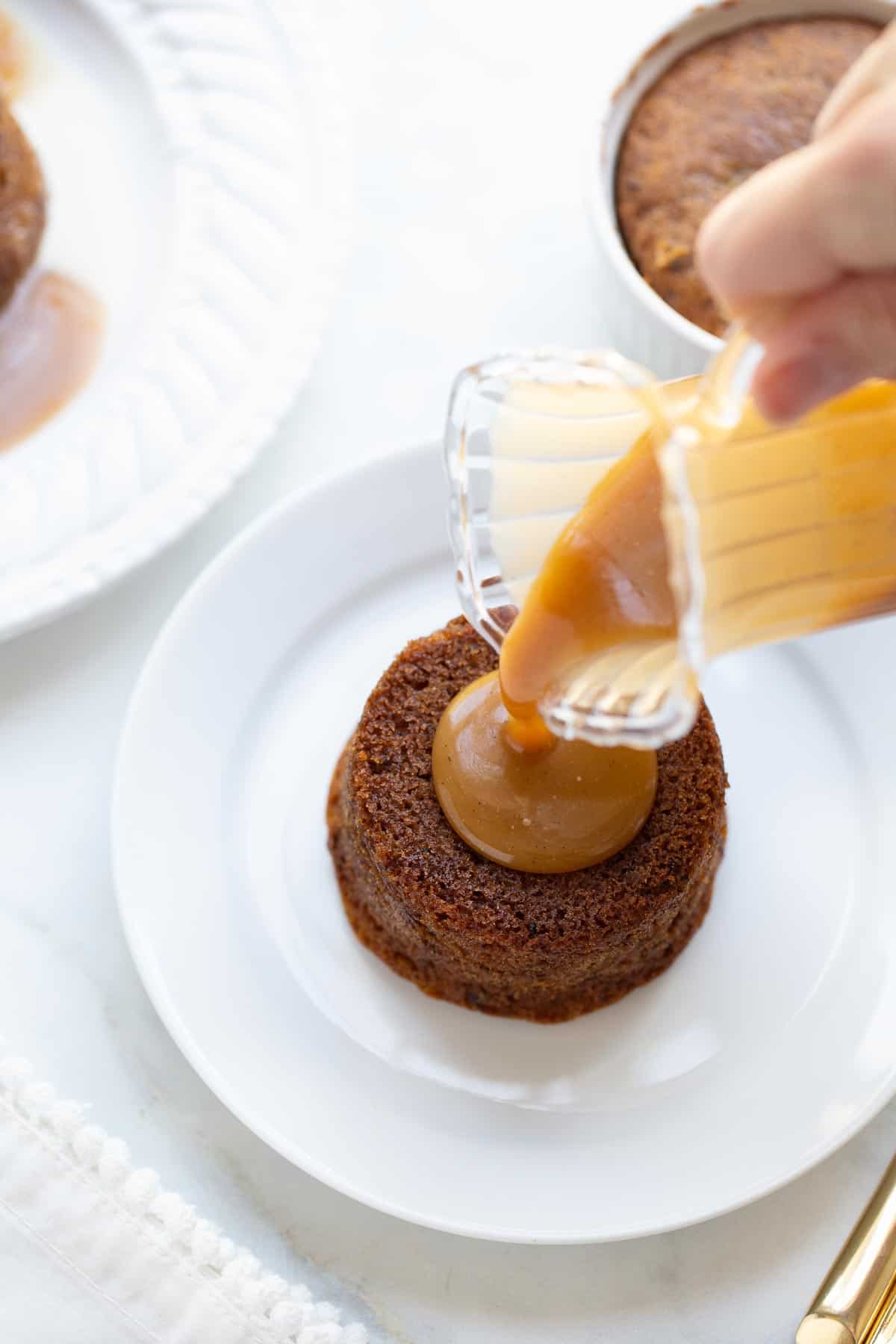 sticky toffee pudding being topped with sauce on white plate