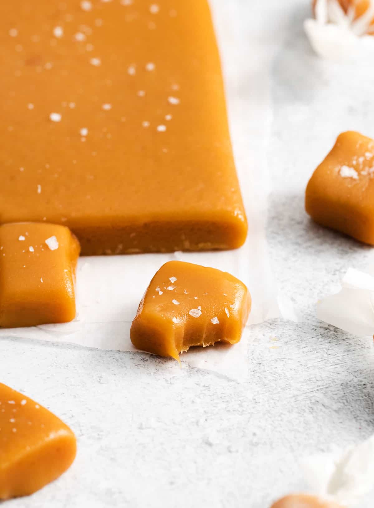 A piece of caramel with a bite taken out of it, and more caramels in the background