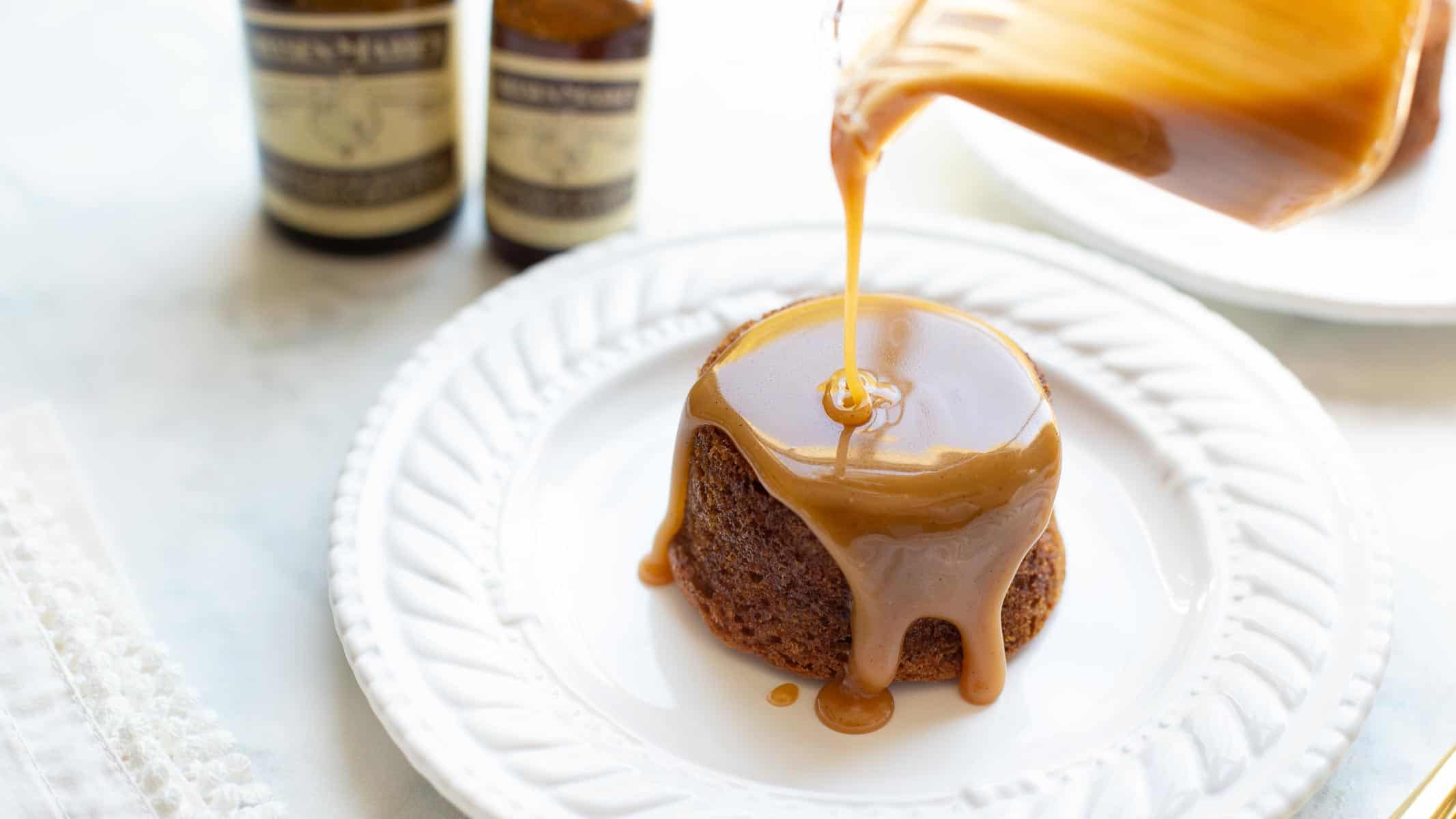 caramel sauce being poured over toffee pudding on white plate